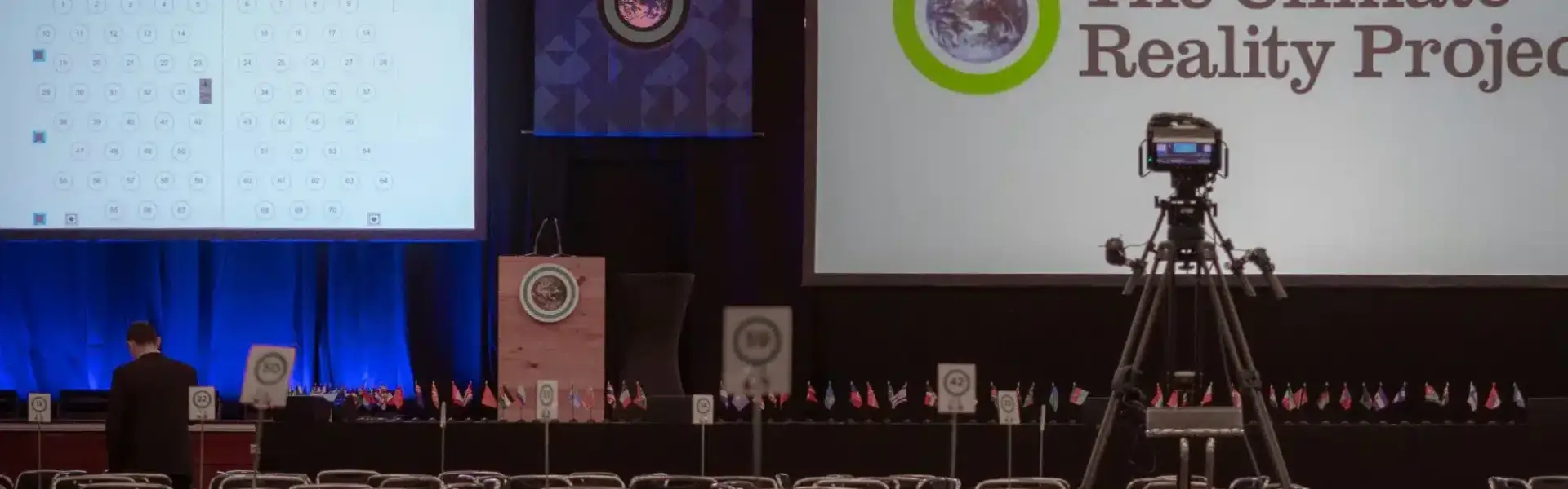 Salle de conférence avec tables rondes, écrans de scène, drapeaux et caméras avant une conférences durabilité 2026.