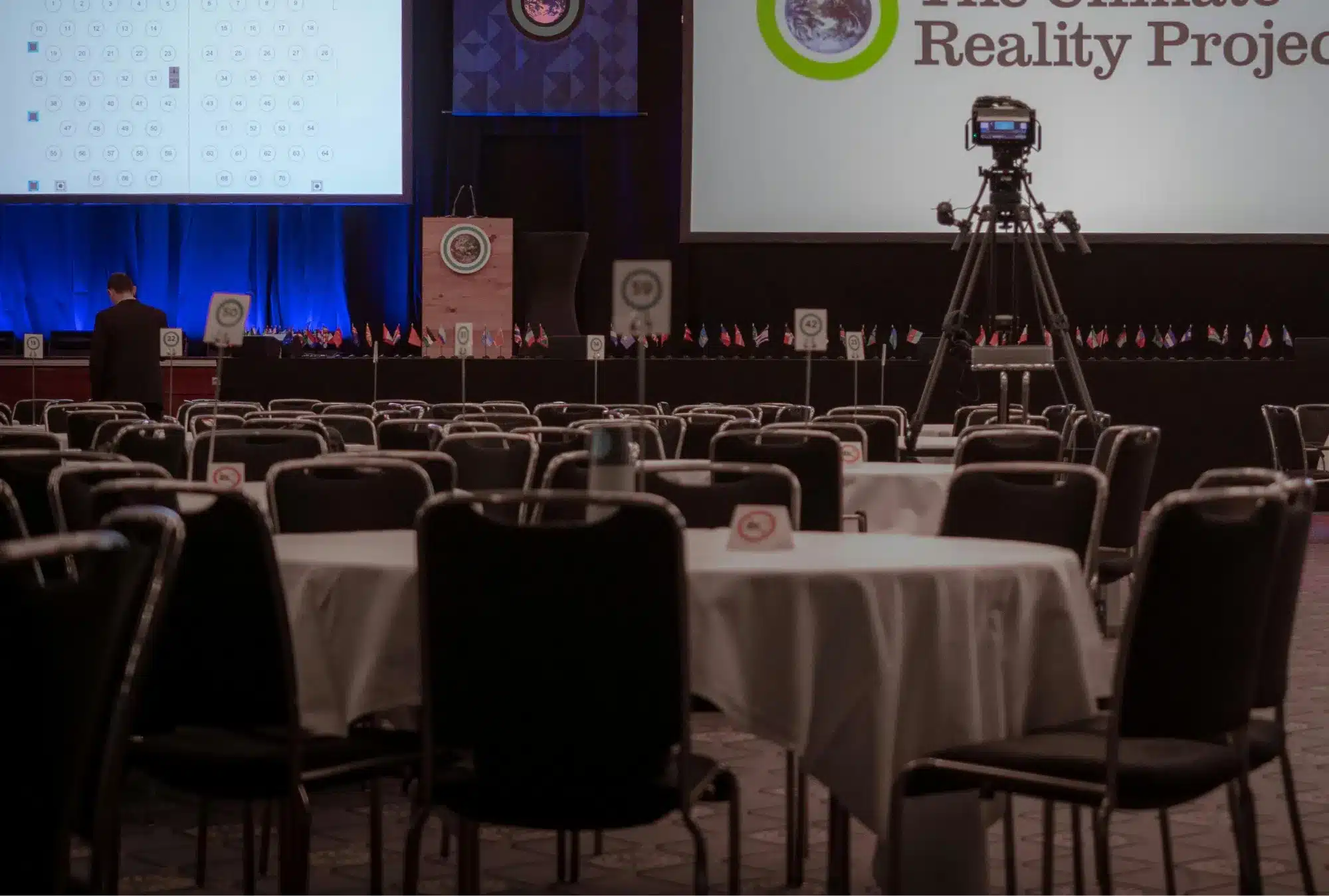 Salle de conférence avec tables rondes, écrans de scène, drapeaux et caméras avant une conférences durabilité 2026.