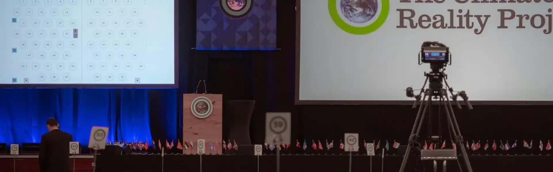Conference hall with round tables, stage screens, flags and camera setup before a sustainability conferences in 2026.